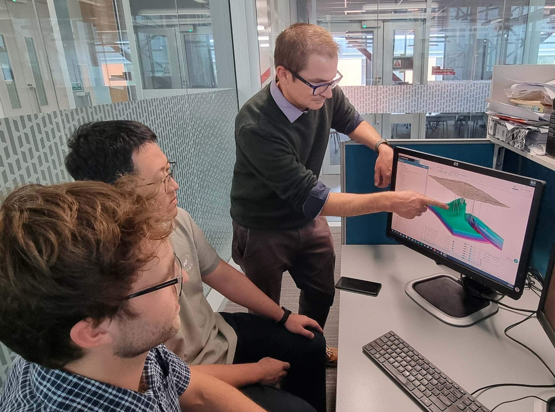 A photo of three men pointing at a computer, showing 3d geological modelling