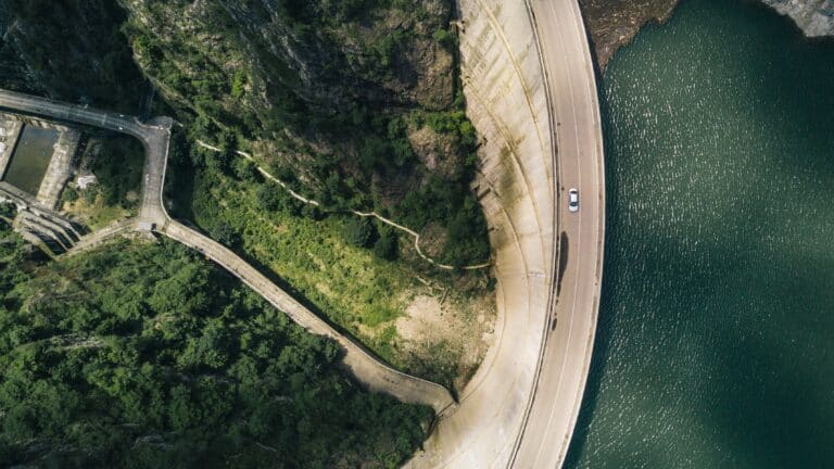 A photograph of a car driving on a winding road atop a dam wall