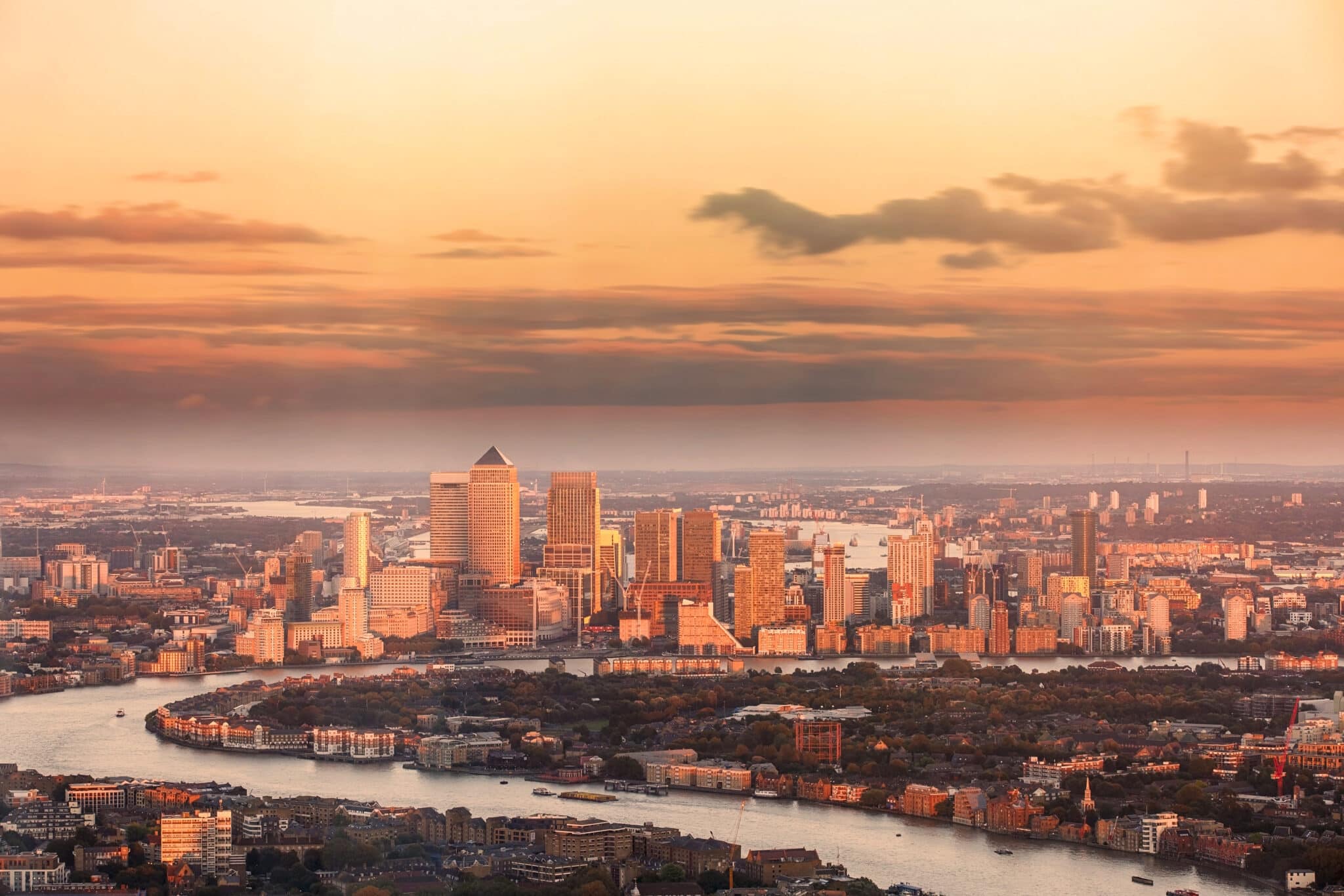 Aerial view of east London financial district of Canary Wharf Docklands circled by Thames river, with buildings illuminated by colourful sunset